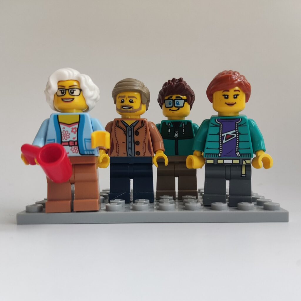 Minifiguren von Susan, Kai, Dave und Anita stehen gestaffelt nebeneinander auf einer grauen Klemmbausteinplatte.
